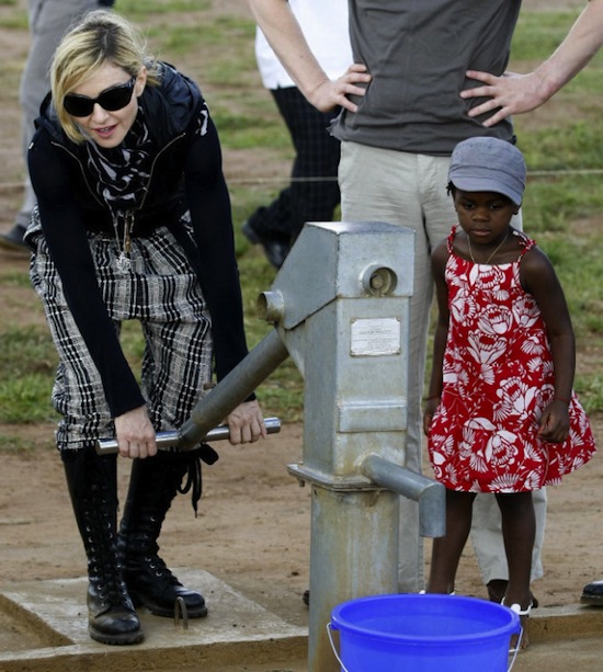 Madonna pumps water from a hand pump next to her adopted Malawian child Mercy James during a visit to Gumulira village